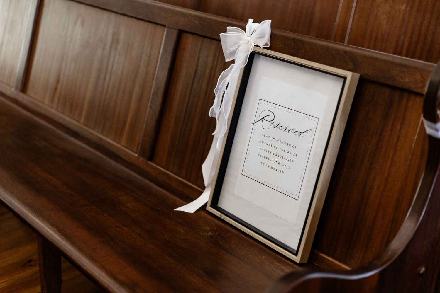 A framed reserved sign with a white bow tied to it sits on a wooden church pew.
