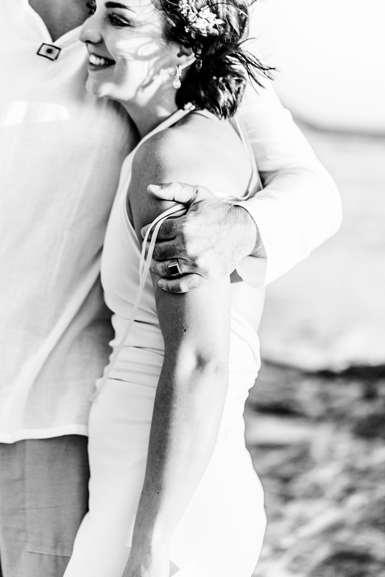 Black and white intimate wedding photo showing a romantic embrace on a beach with the bride in white dress.