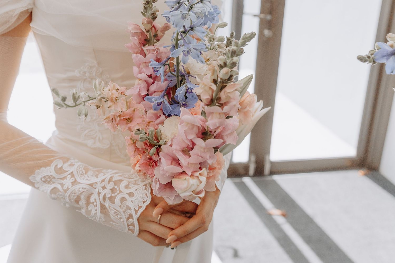Delicate pastel floral arrangements in pink and blue hues displayed in vintage wooden boxes near a sunlit window.