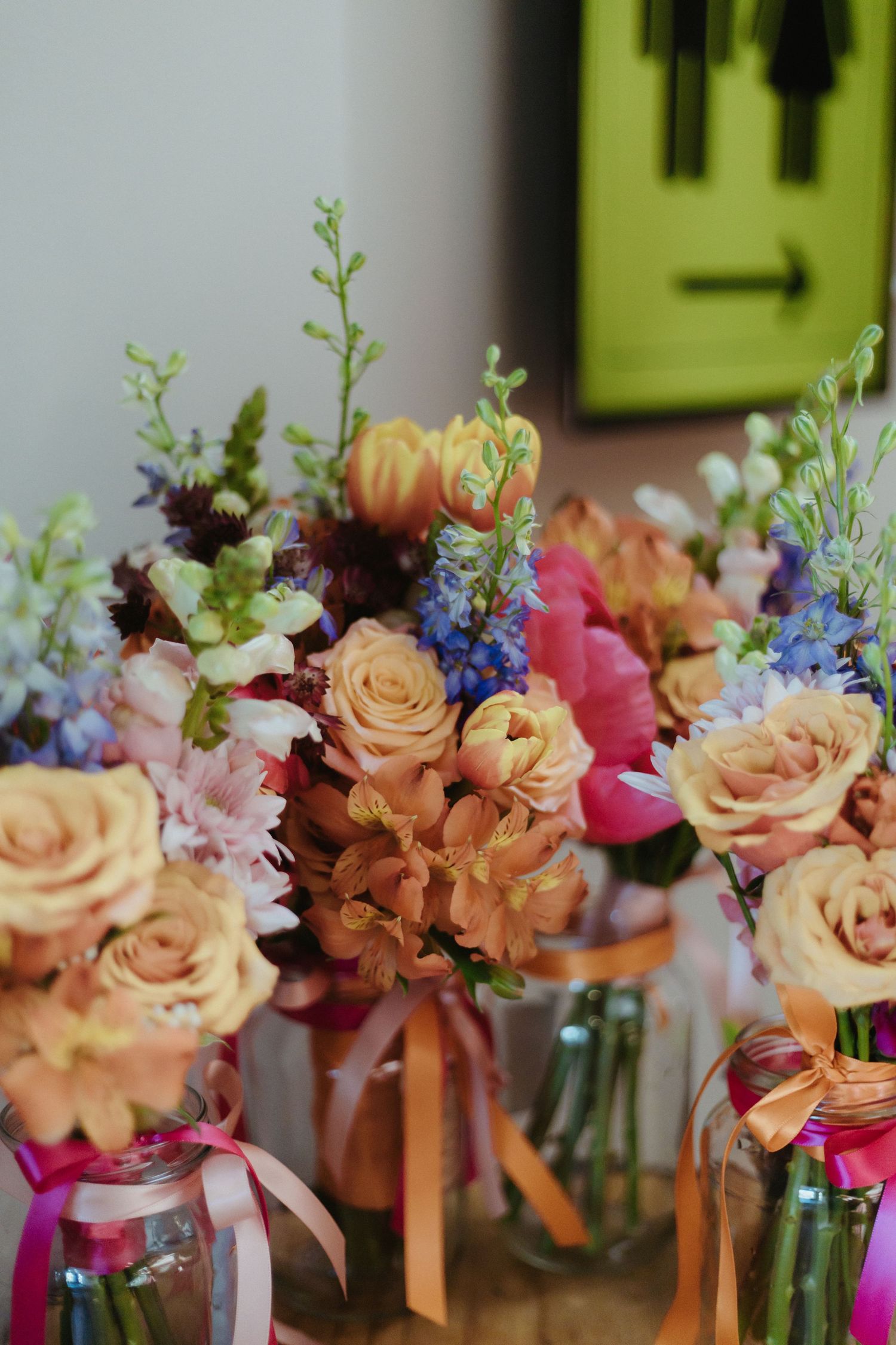 A row of delicate floral arrangements with peach roses and blue accents in small glass vases tied with ribbons.
