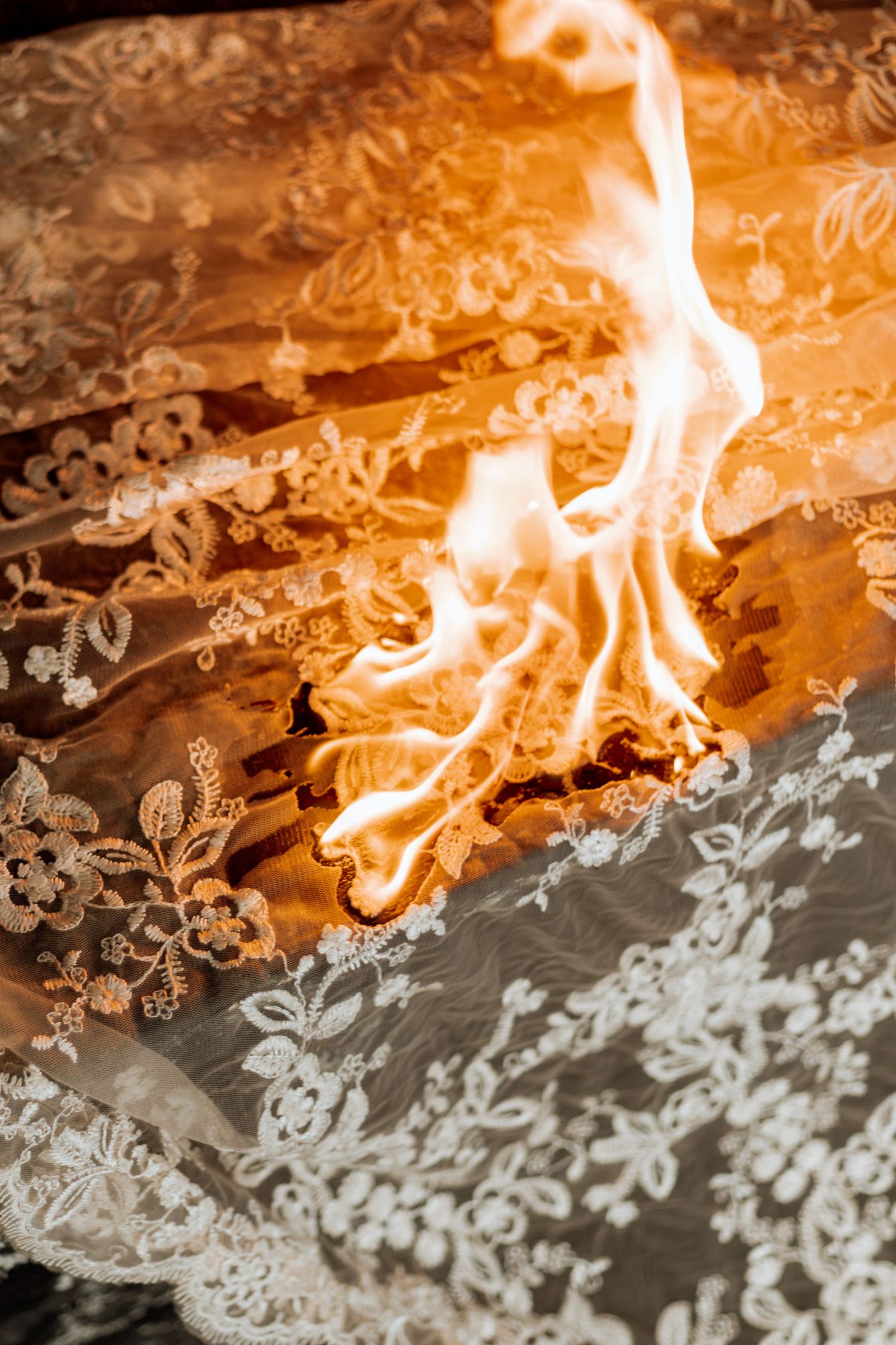 Fire engulfs a textured backdrop creating dramatic orange flames against a lace or decorative pattern surface.