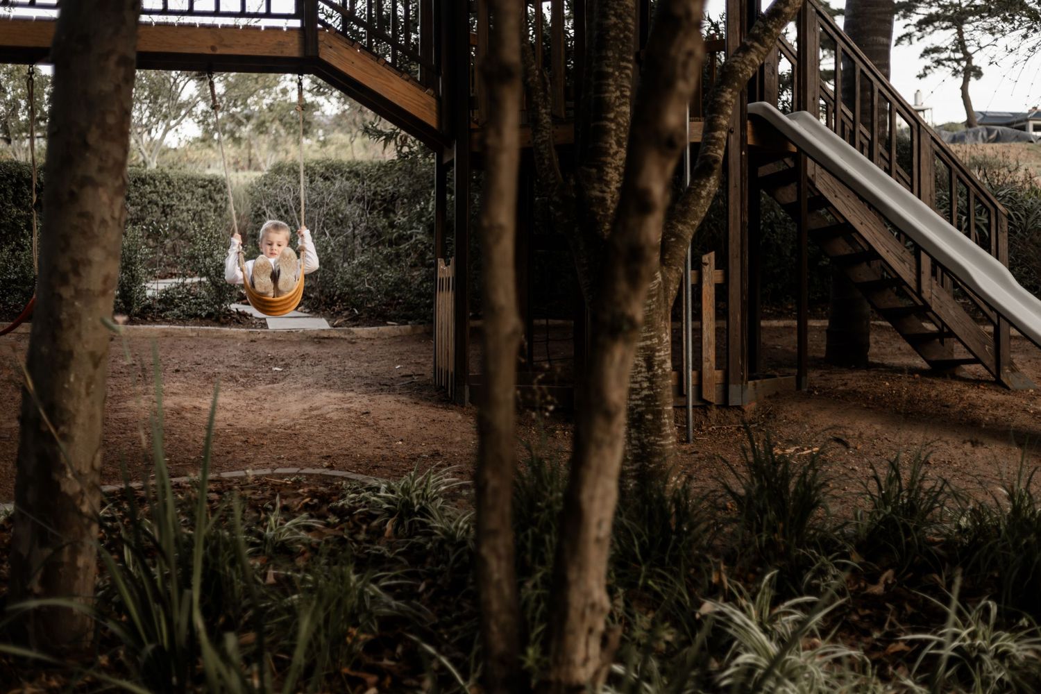 A rustic wooden staircase leads up through a wooded area with trees and natural landscaping.