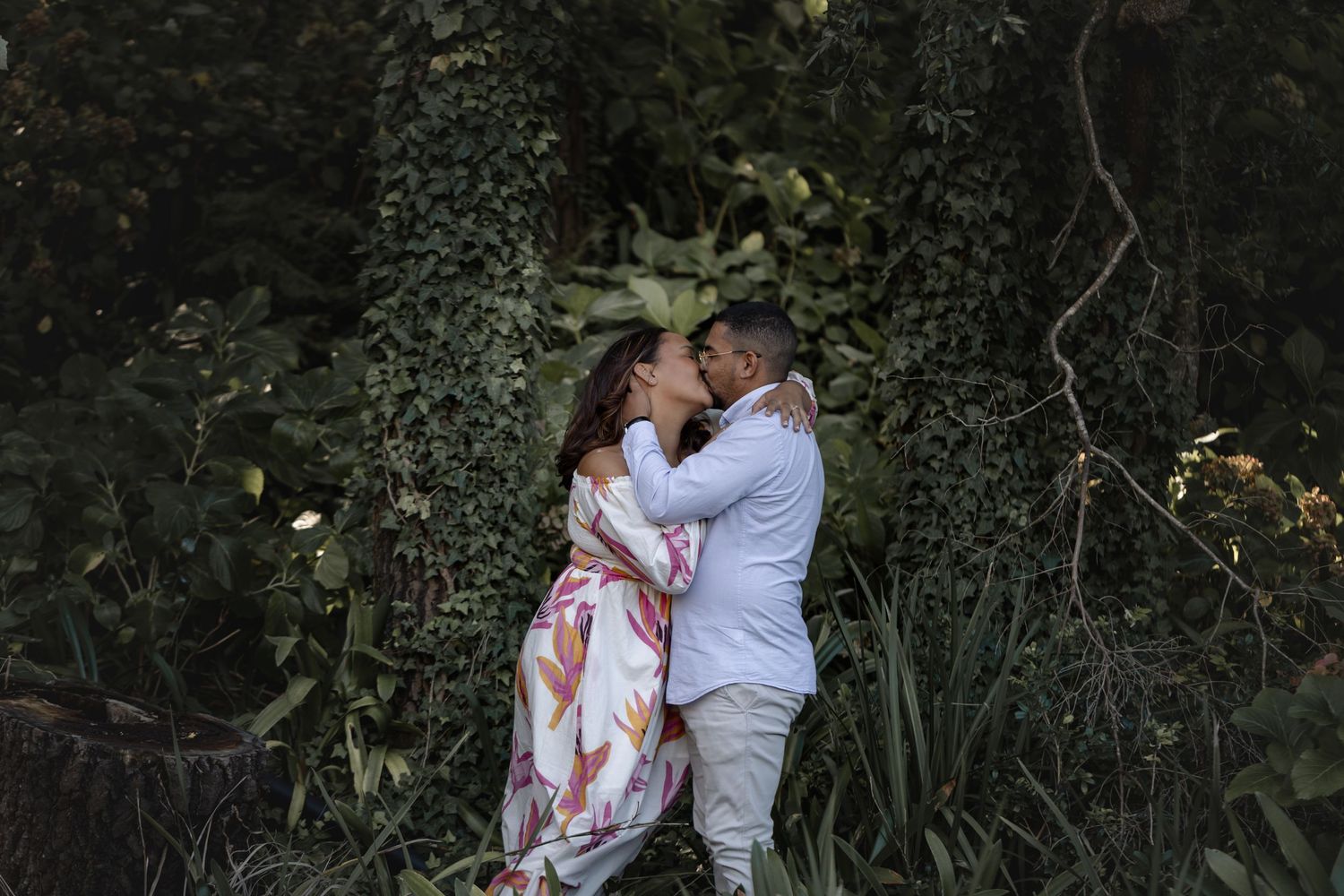 A couple in white and floral attire dance together in a romantic outdoor setting.
