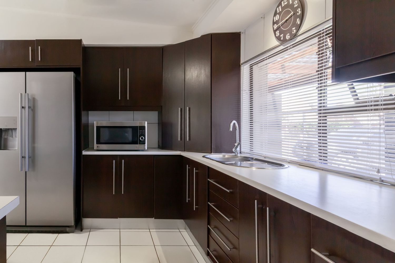 Modern kitchen with dark espresso cabinets, stainless steel appliances, and white countertops along a windowed wall.
