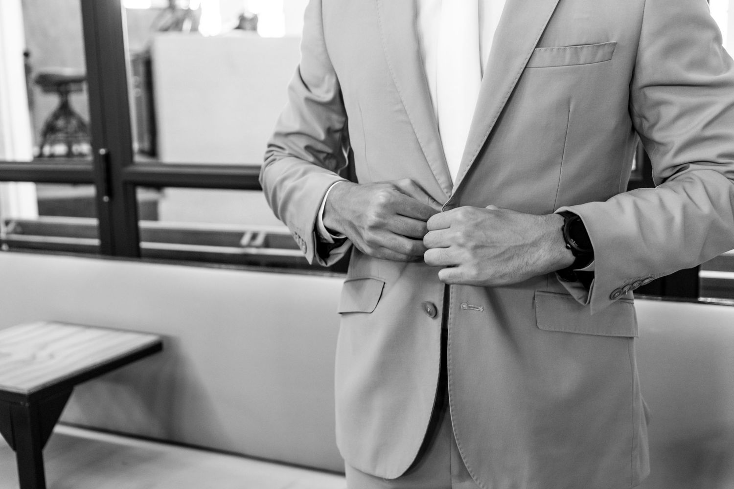 Professional in a light gray suit jacket adjusts their blazer while wearing a smartwatch in a modern office setting.