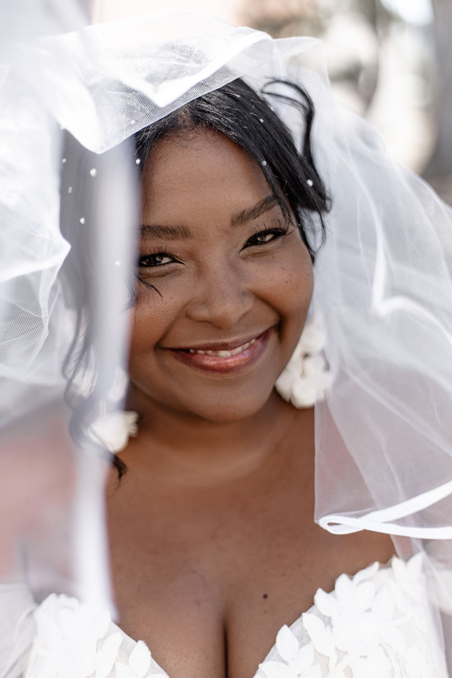 A joyful bride wearing a traditional white wedding veil and dress smiles warmly at the camera.
