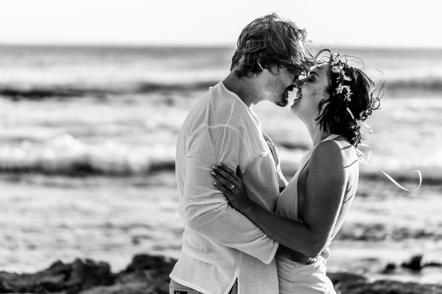 A romantic couple embraces on the beach in a black and white photo series showing intimate moments by the ocean.