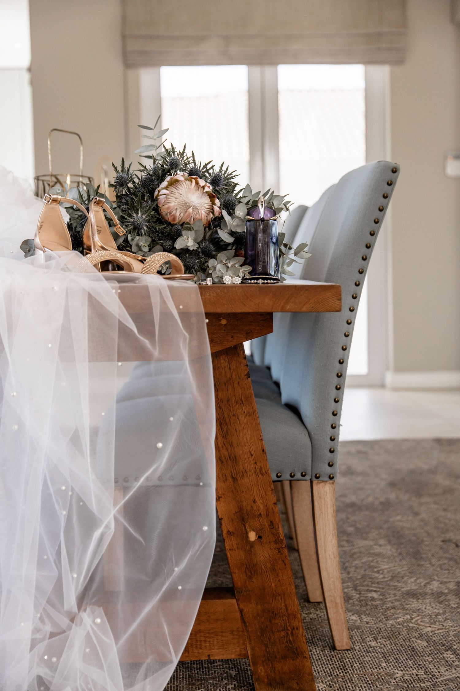 Elegant dining chairs with white tulle decorations and greenery arrangements in a modern room with large windows.