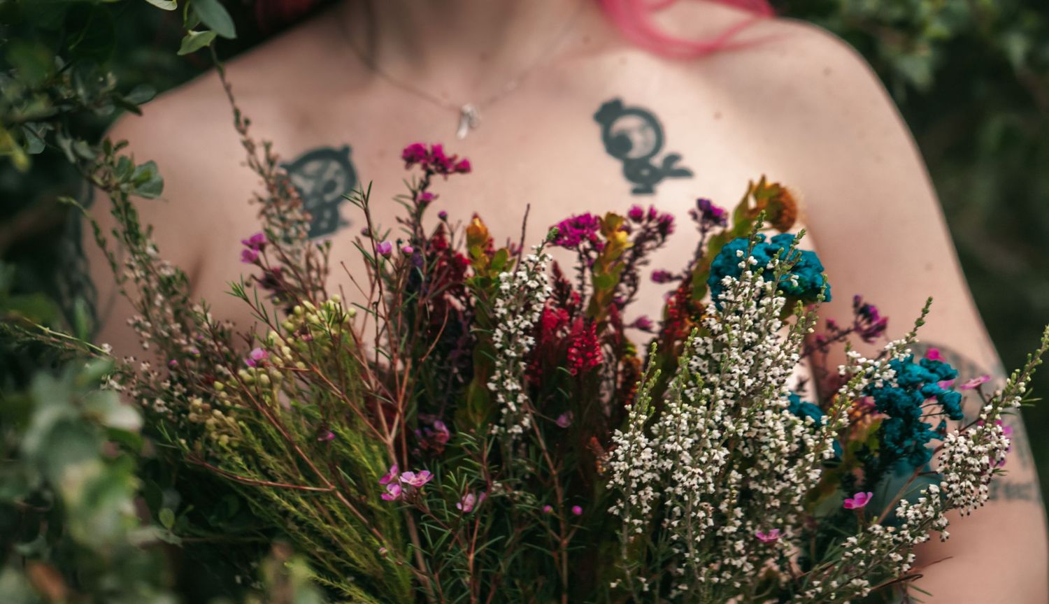 A rustic wildflower bouquet with dried flowers in red, blue and white held against a natural outdoor background.