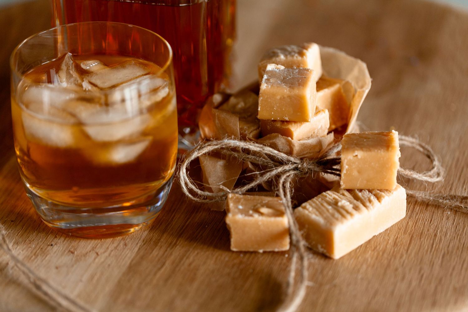 Cubes of brown sugar and glasses of whiskey arranged on a rustic wooden surface in warm lighting.
