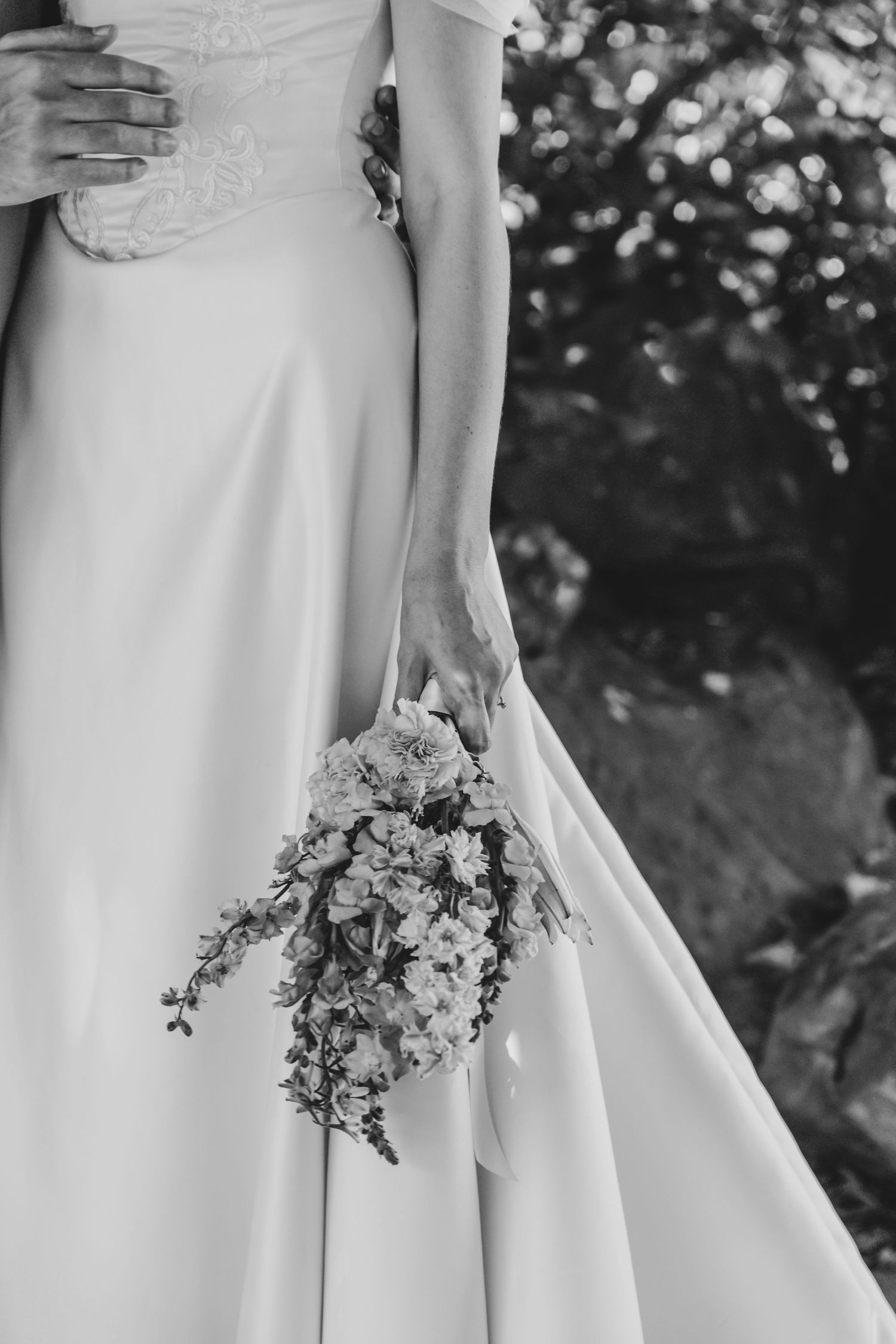 Black and white photo of bridesmaids in white dresses holding small floral bouquets in a line.