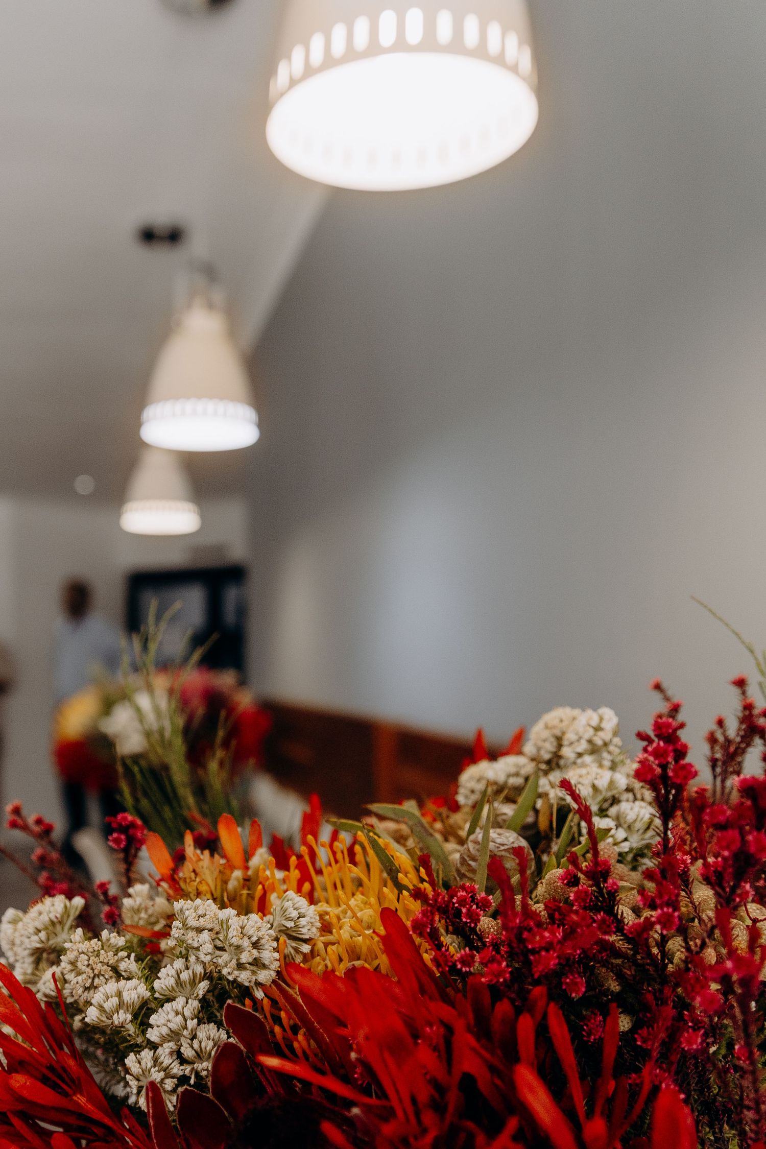 Vibrant red and white dried flowers arranged under modern pendant lights in an interior space.
