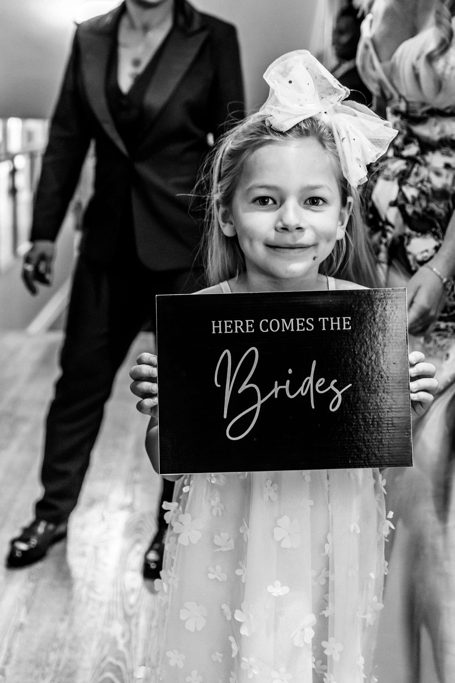Black and white wedding ceremony photos showing a decorative 'Here Comes the Bride' sign and joyful moments.