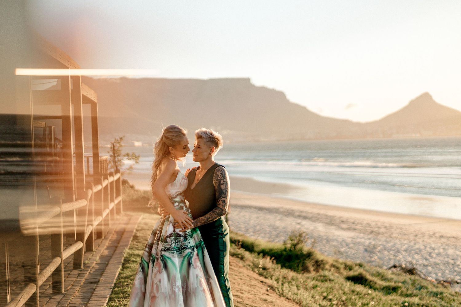 Romantic couple embraces on beach path during golden sunset with ocean waves in background.