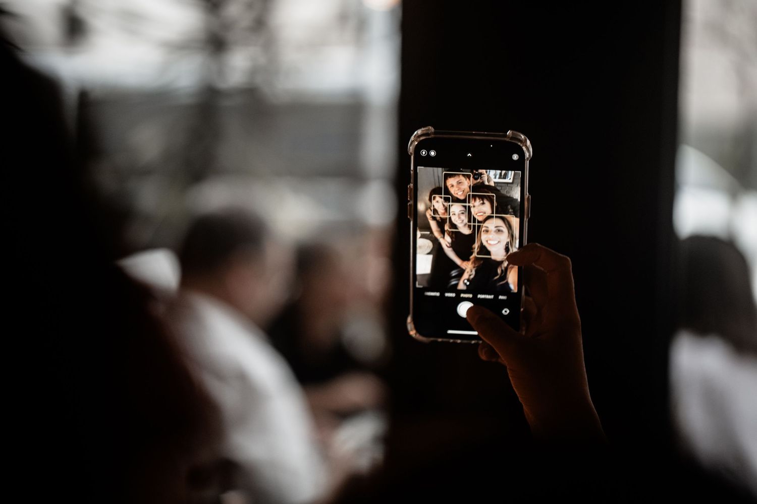 Hand holding smartphone displaying selfie photo of smiling people at social gathering.