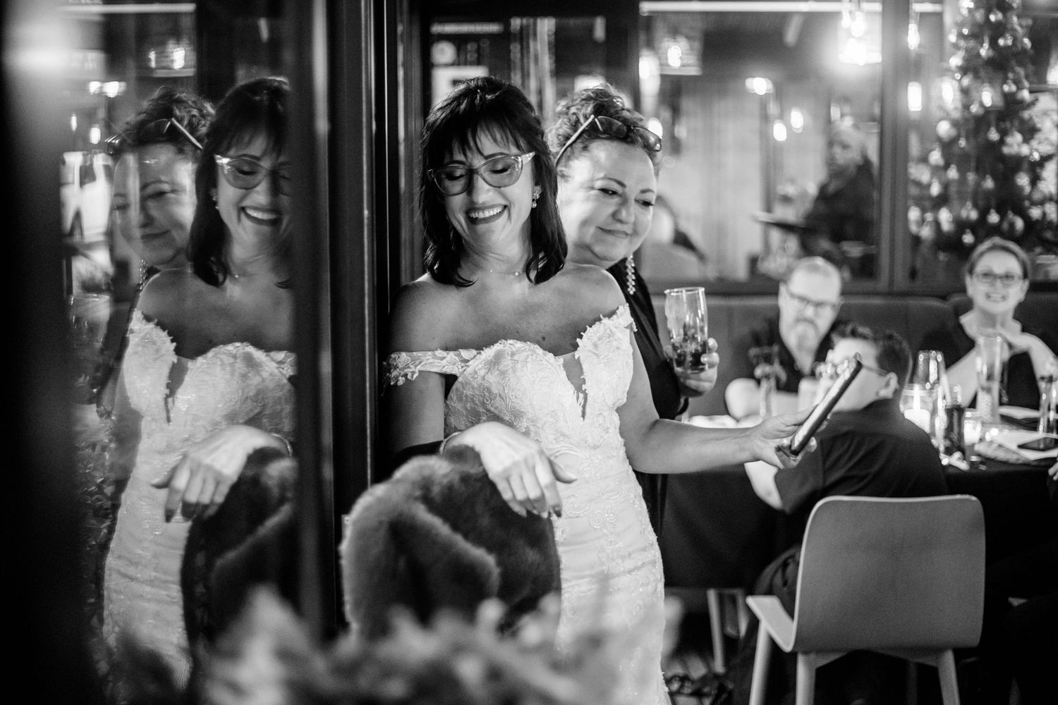 A black and white wedding reception photo showing a couple celebrating with guests in an elegant restaurant setting.