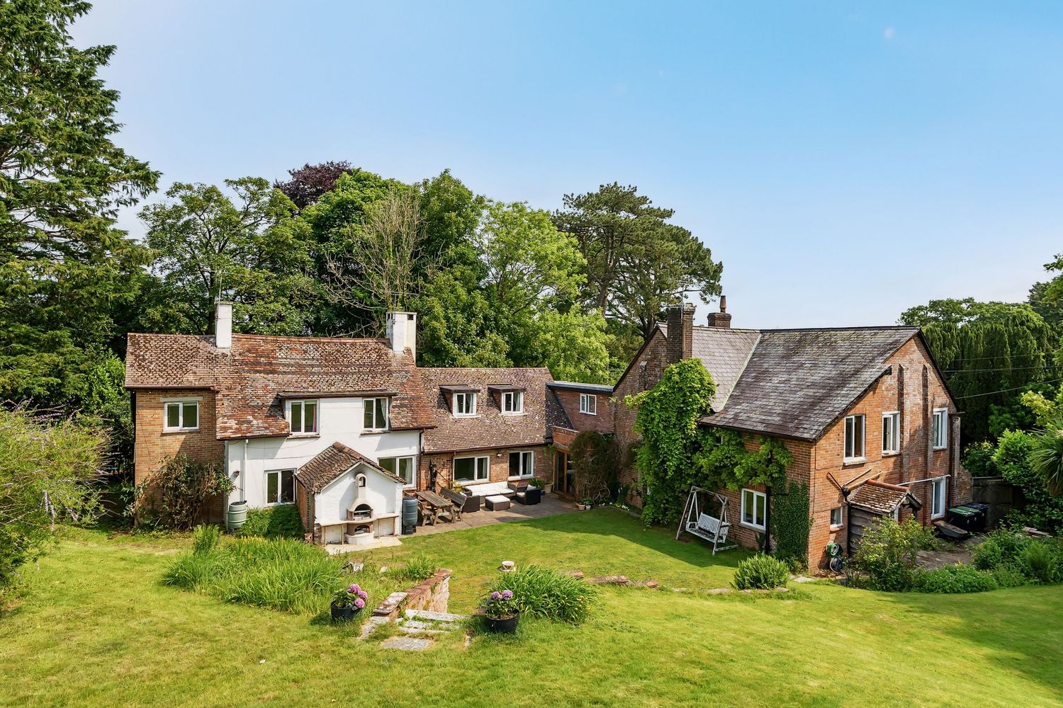 A panoramic view of an old brick farmhouse among green lawns and trees in a rural countryside setting.