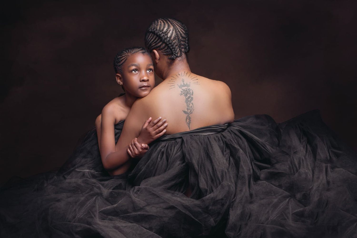 Intimate portrait featuring a parent and child embracing while wearing flowing black tulle against dark background.