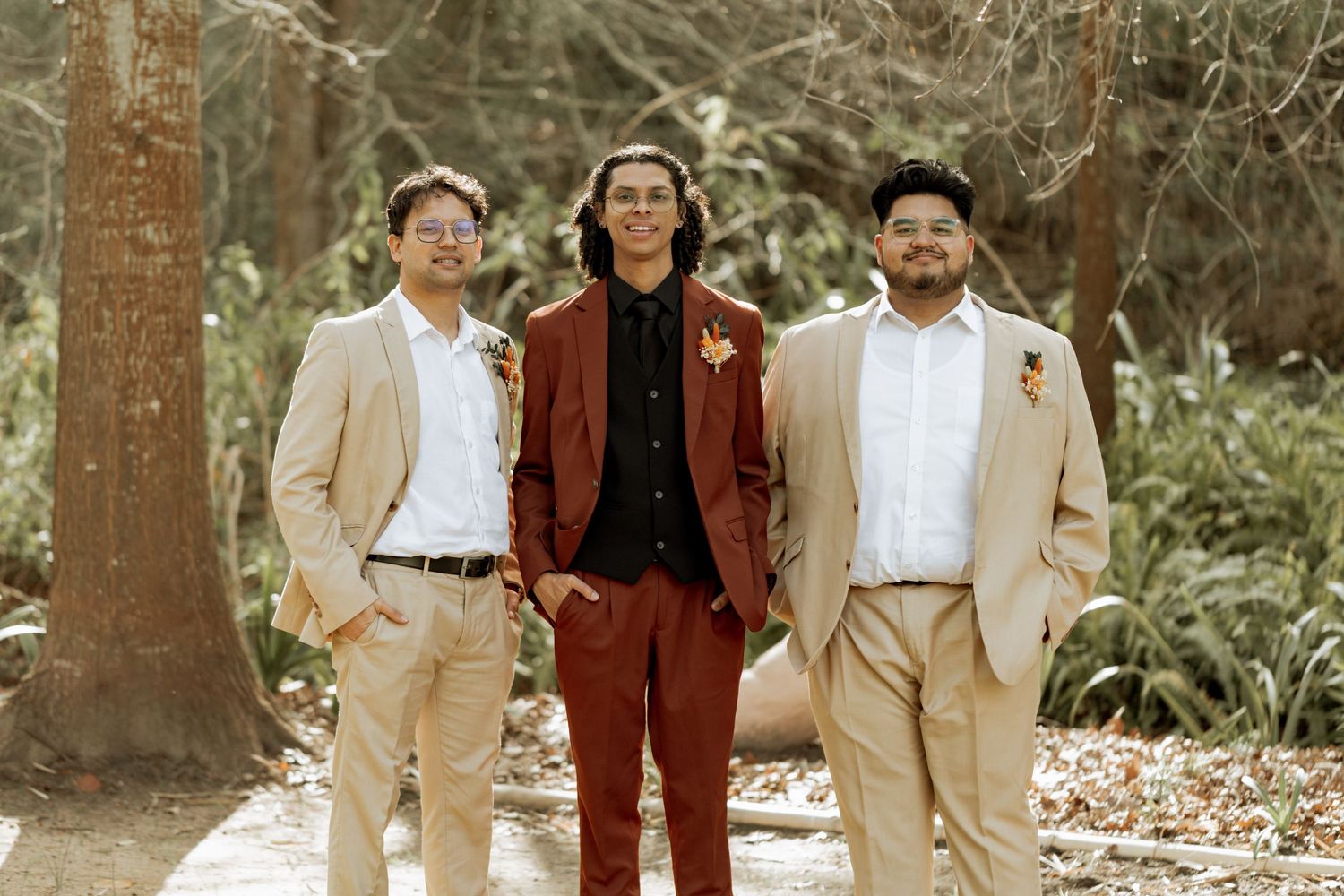 A group wearing coordinated brown, tan and white outfits poses together in a wooded outdoor setting.