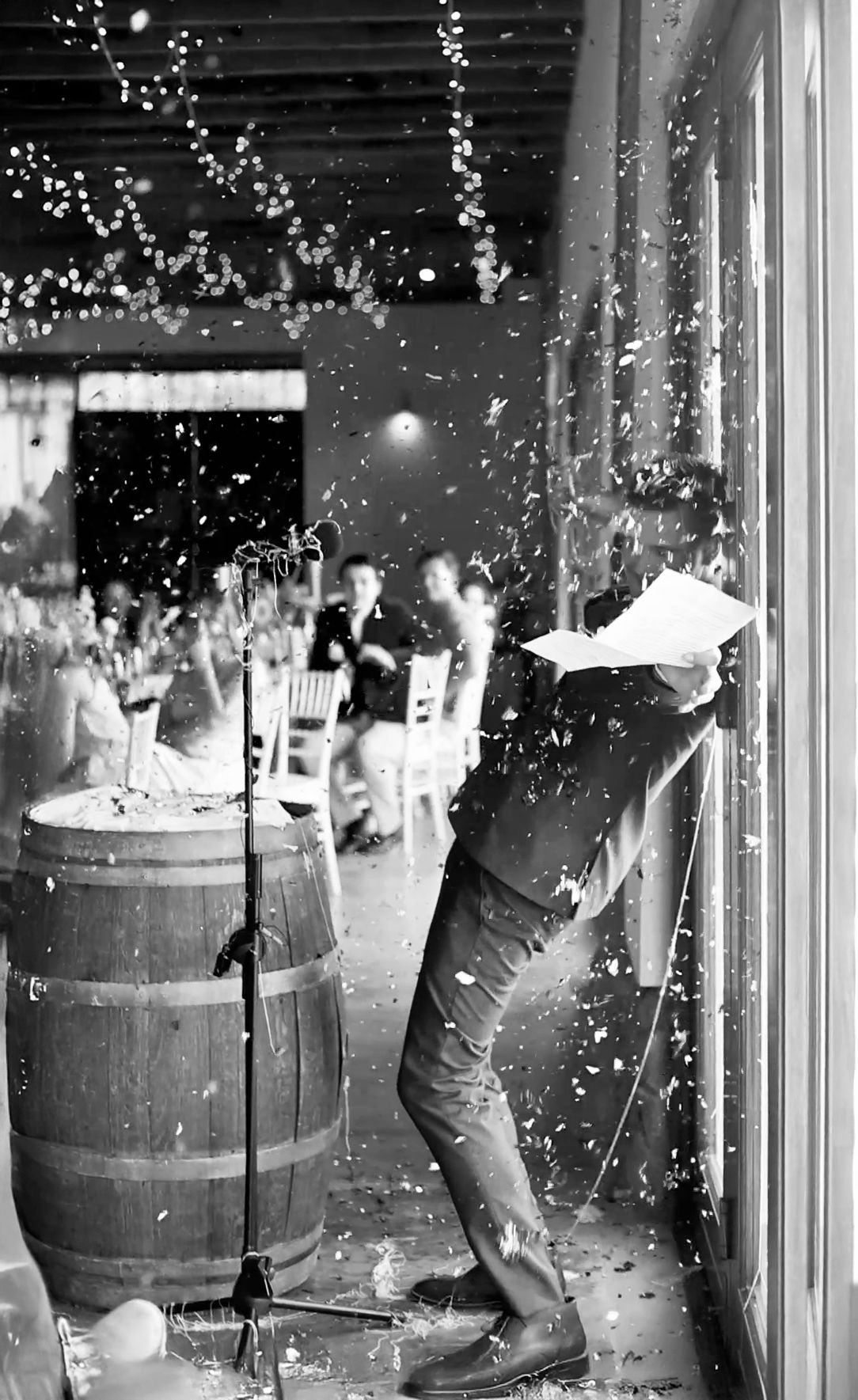 Black and white photo of people having a snowball fight between wooden barrels with snow flying through the air.