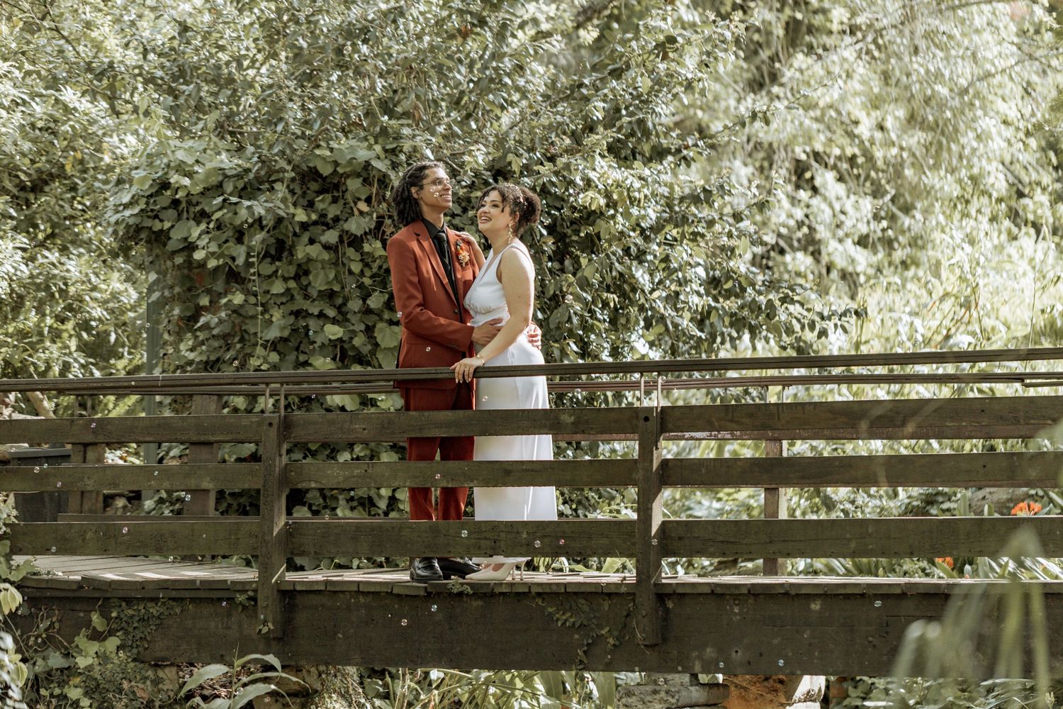 Outdoor engagement photo session on a rustic wooden bridge surrounded by lush green trees and natural scenery.