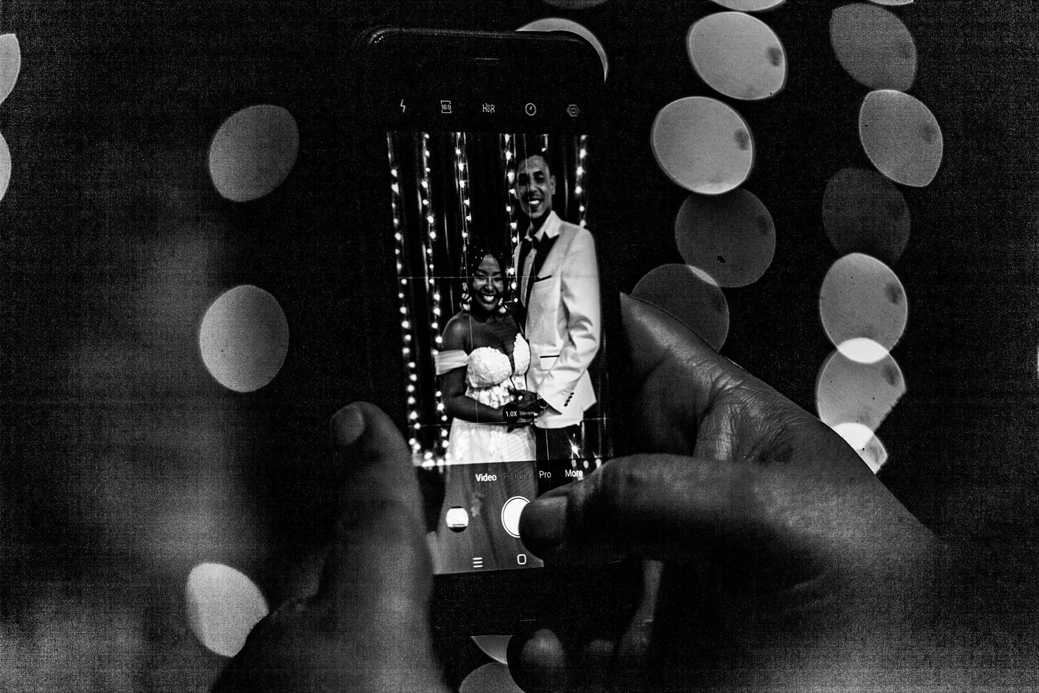 A black and white photograph showing glowing bokeh lights and a silhouette sitting against a backlit backdrop.