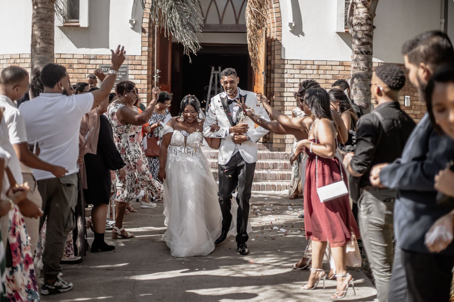Wedding guests throw confetti and celebrate as newlyweds exit rustic brick church after ceremony.