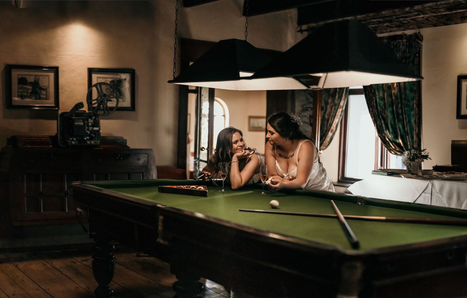 Three dimly lit billiard tables in a dark game room with moody lighting and wall decor.