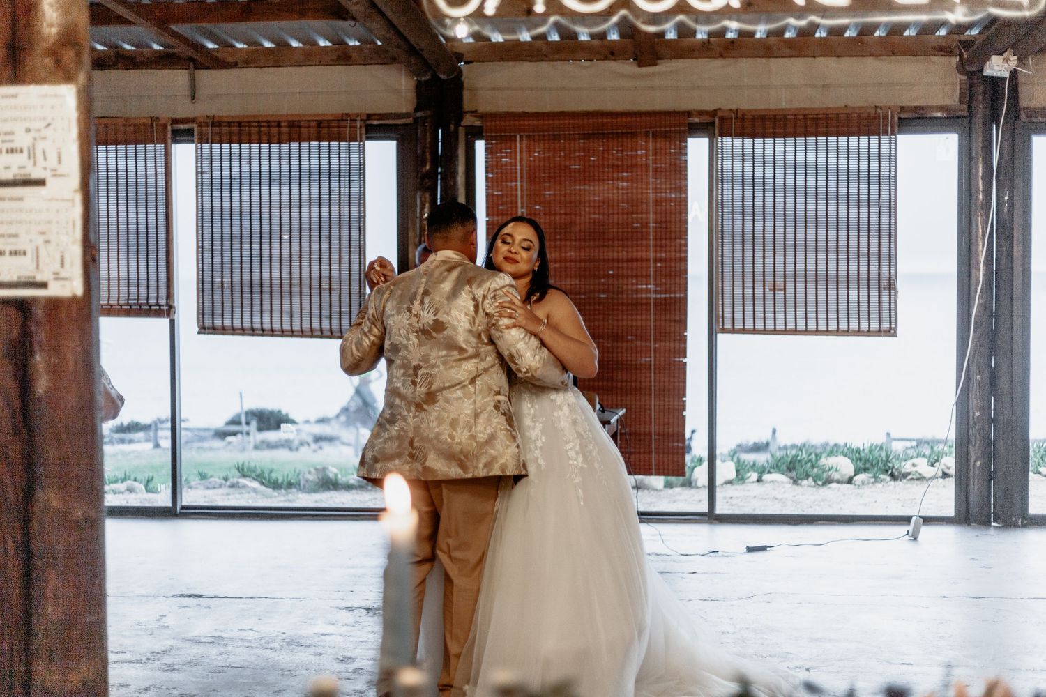 A couple shares a joyful moment laughing together at a rustic venue with wooden beams and corrugated metal walls.
