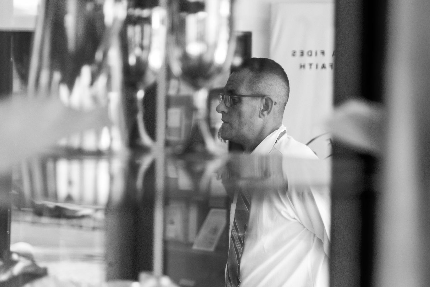A person in glasses and white shirt gazes through a window in black and white photography.