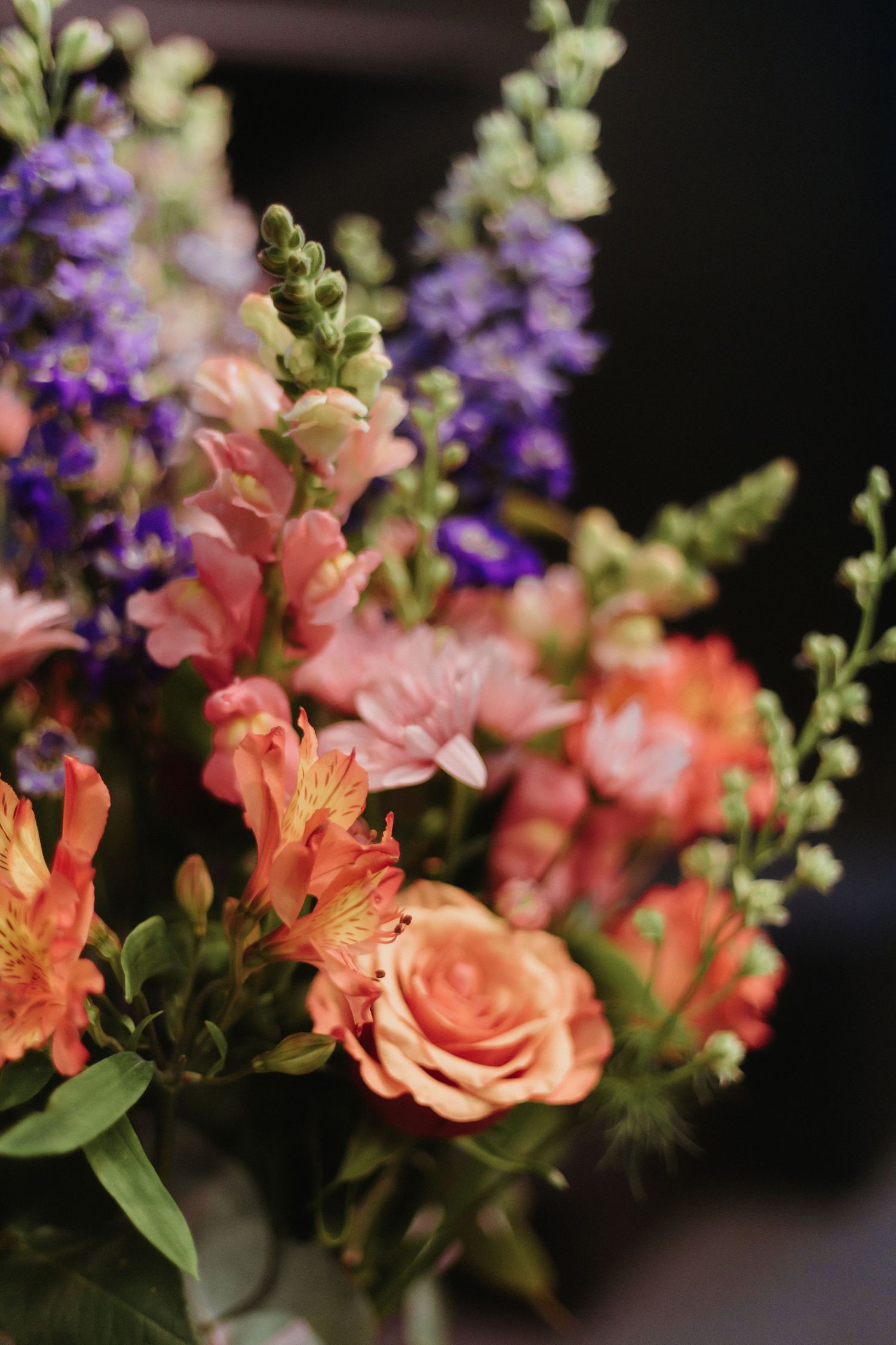 Close-up view of pink alstroemeria and purple delphinium flowers arranged against a dark background.