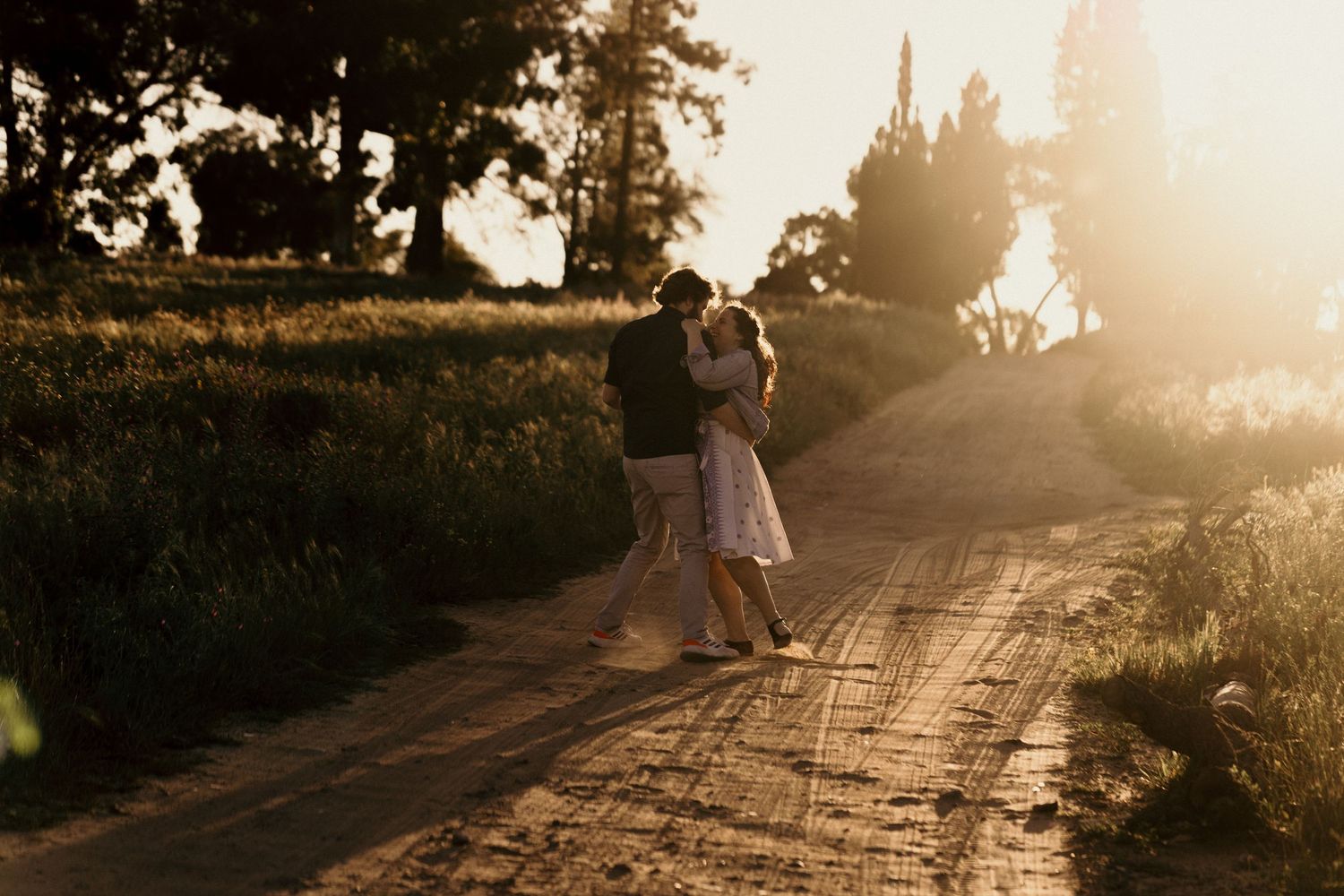 Silhouetted figures walking on a dirt path through a garden at sunset with golden light filtering through trees.