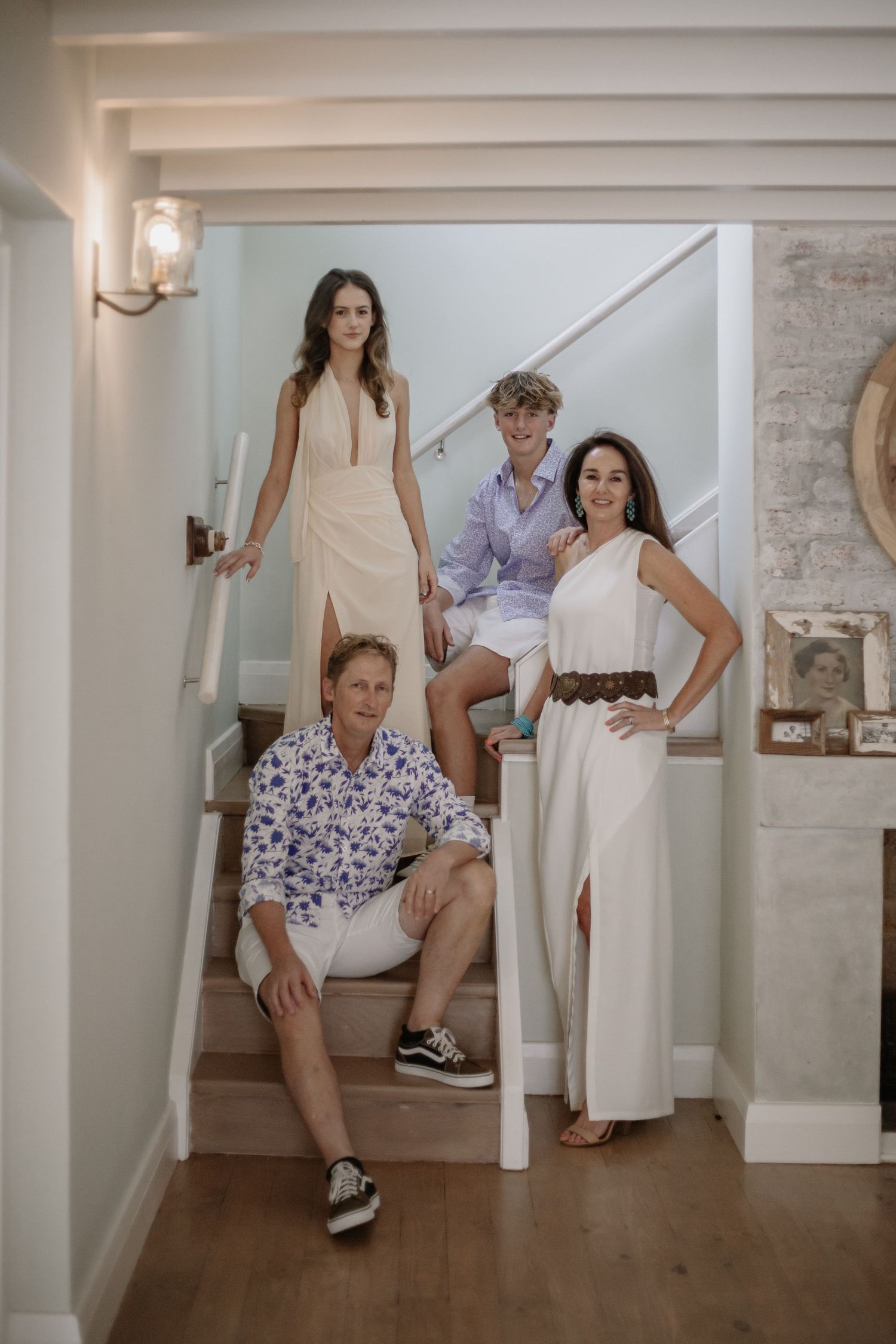 Five women in casual summer attire pose on wooden stairs in a bright interior setting.