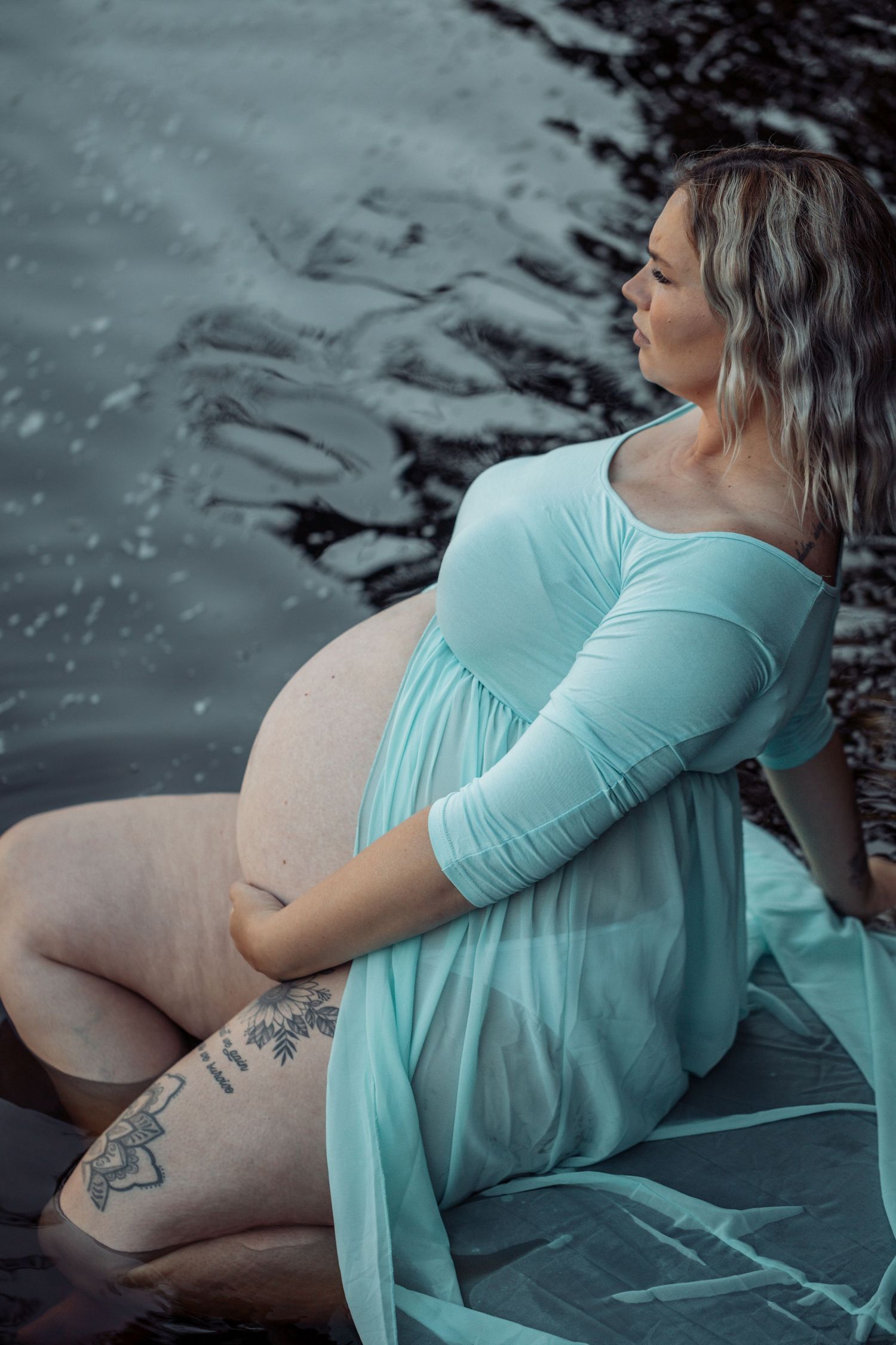 A maternity photoshoot sequence showing a person in a mint green dress sitting on dark rocks near water.