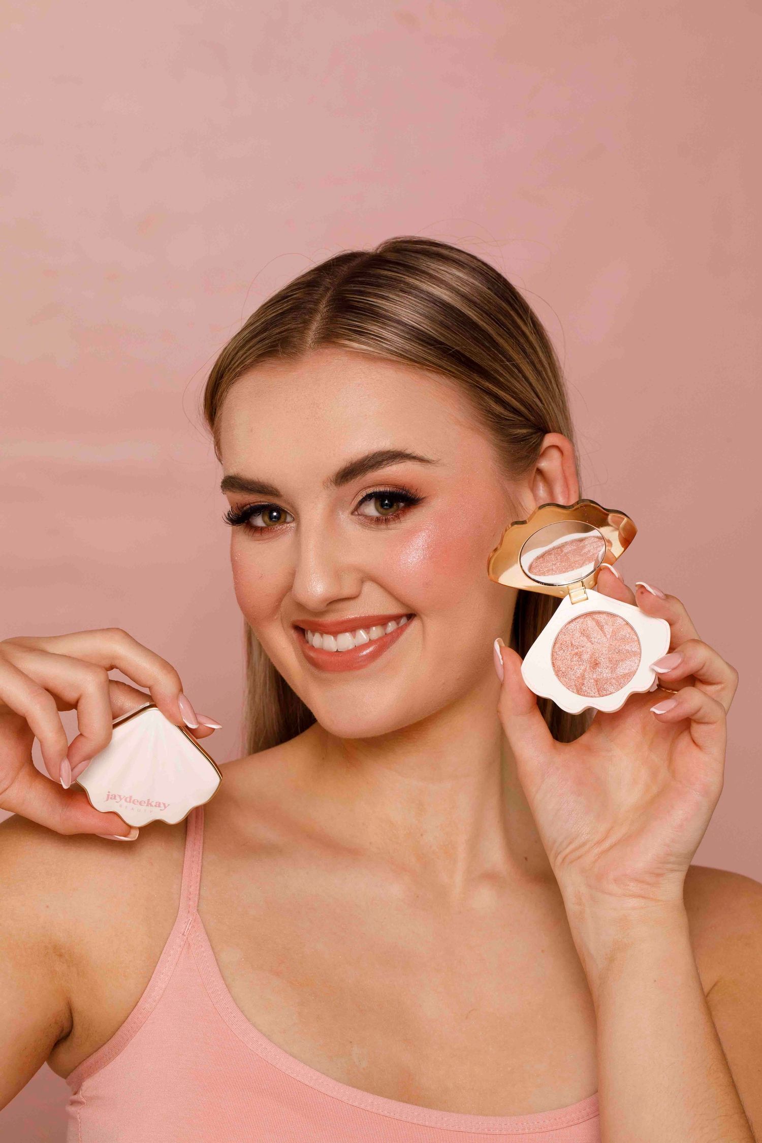 Four sequential photos showing someone holding and displaying a pink frosted cookie against a pink background.