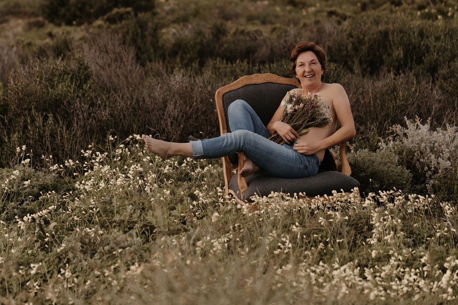 Someone relaxes in a vintage chair among wildflowers and tall grass at golden hour with their dog in their lap.