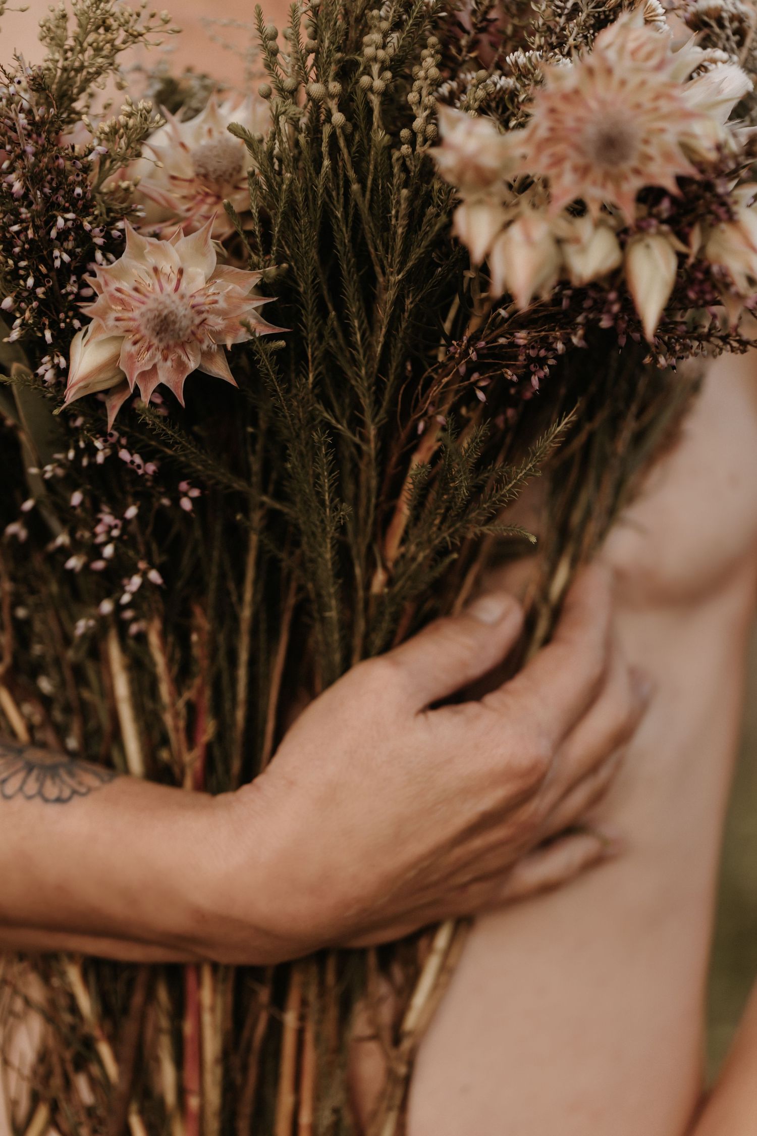Hand holding delicate wildflower bouquet arranged with dried flowers in natural earth tones.