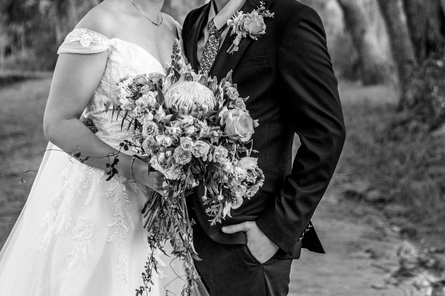 A romantic wedding couple photographed in black and white while holding hands in an outdoor garden setting.