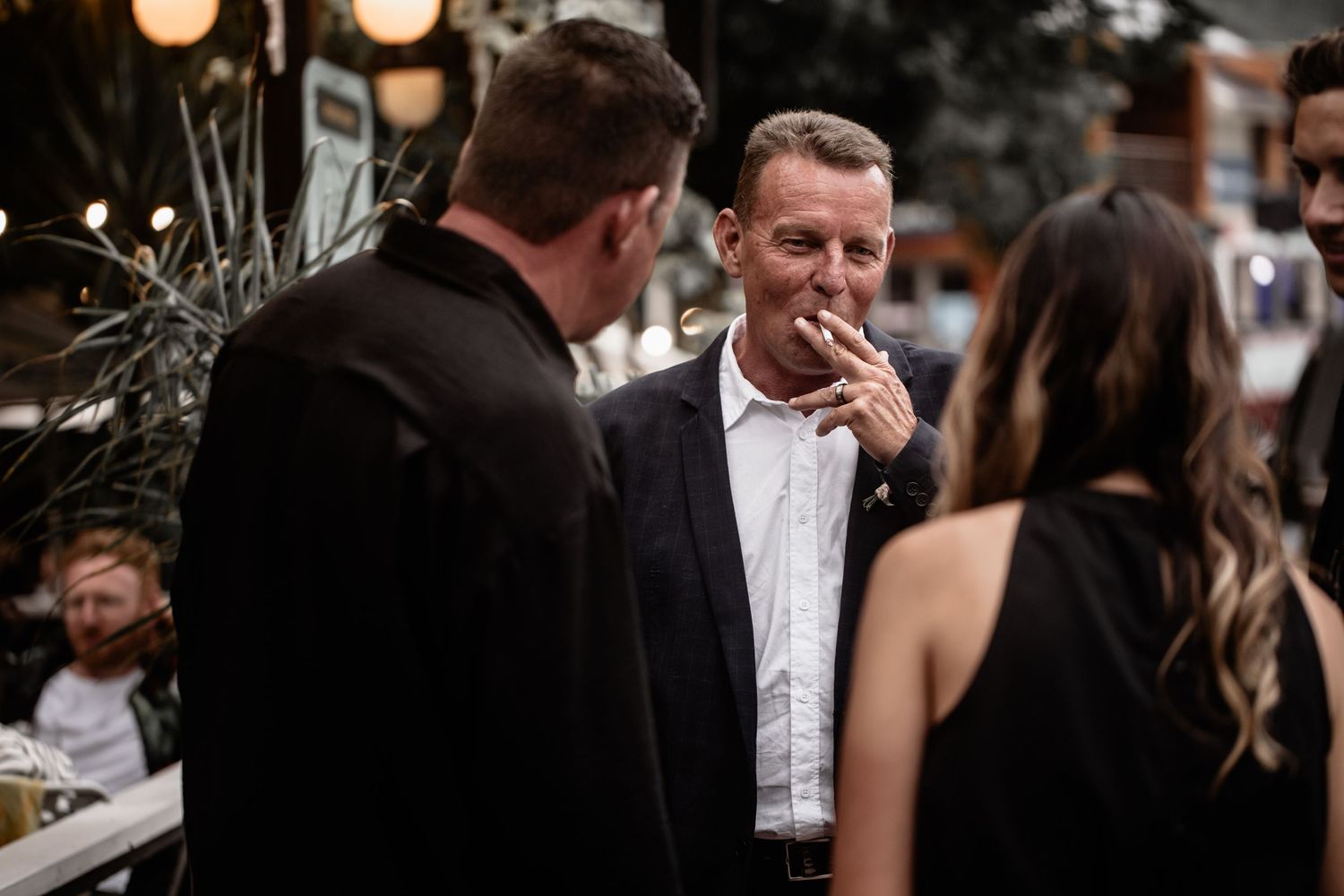 A candid moment at a formal event as guests converse in evening attire with warm lighting in the background.