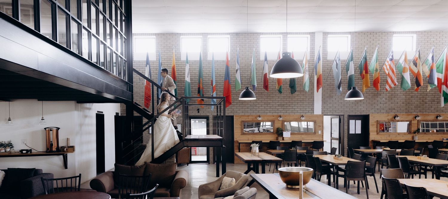 Modern office interior with industrial design features long communal tables and pendant lighting under high ceilings.