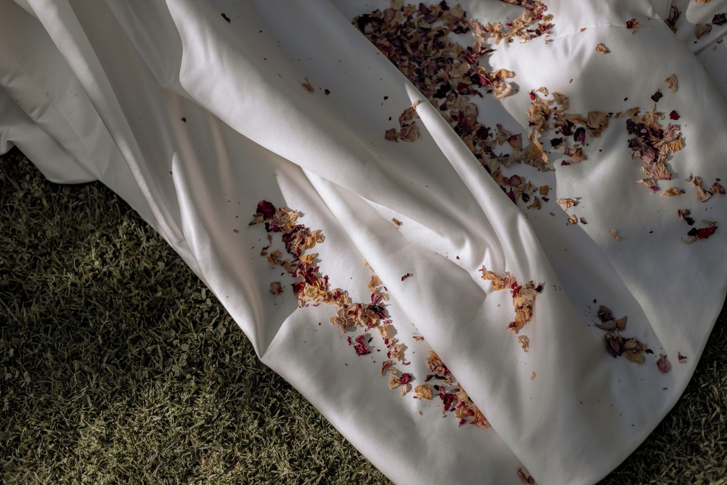 Dried flower petals scattered on white fabric against green carpet, creating a soft romantic composition.