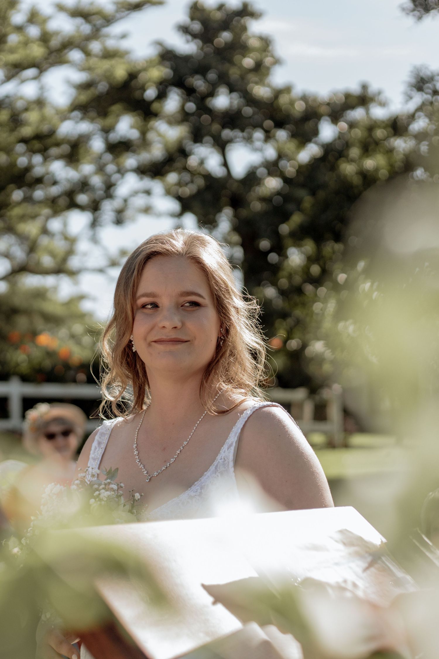 Blonde figure sits among blooming white spring flowers in sunlit garden setting.