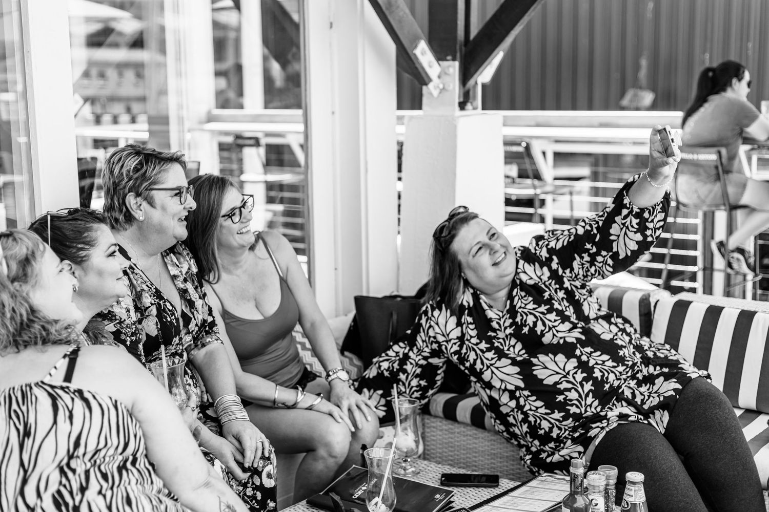 Group of people sitting together and laughing on a covered patio with striped cushions.