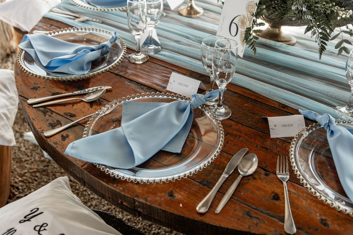 Elegant rustic table setting with pale blue napkins and crystal glasses arranged on a wooden dining table.