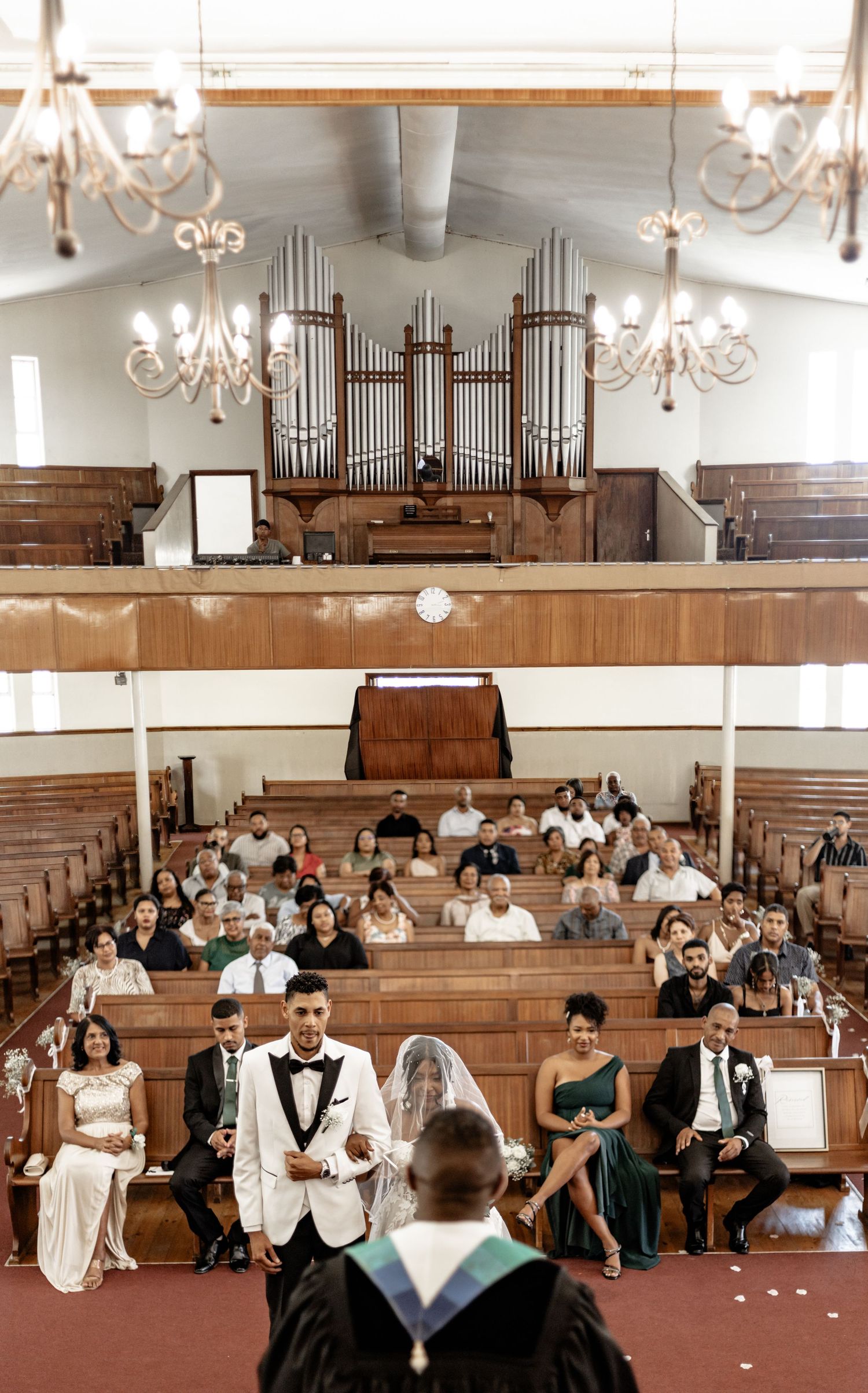 Interior of a church with elegant chandeliers, wooden pews and a pipe organ during a wedding ceremony.