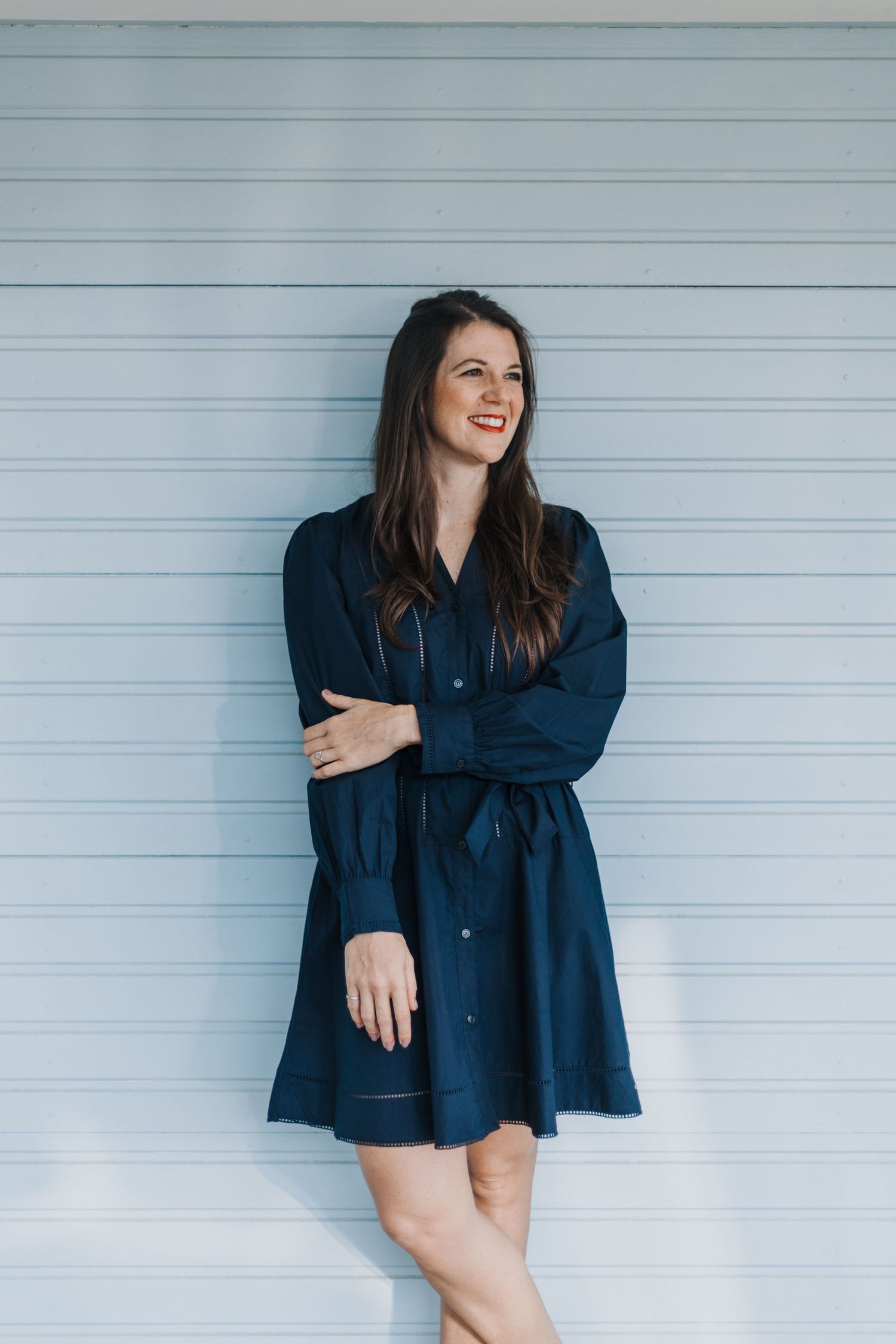 Navy blue shirt dress styled casually against light blue wall with relaxed pose.
