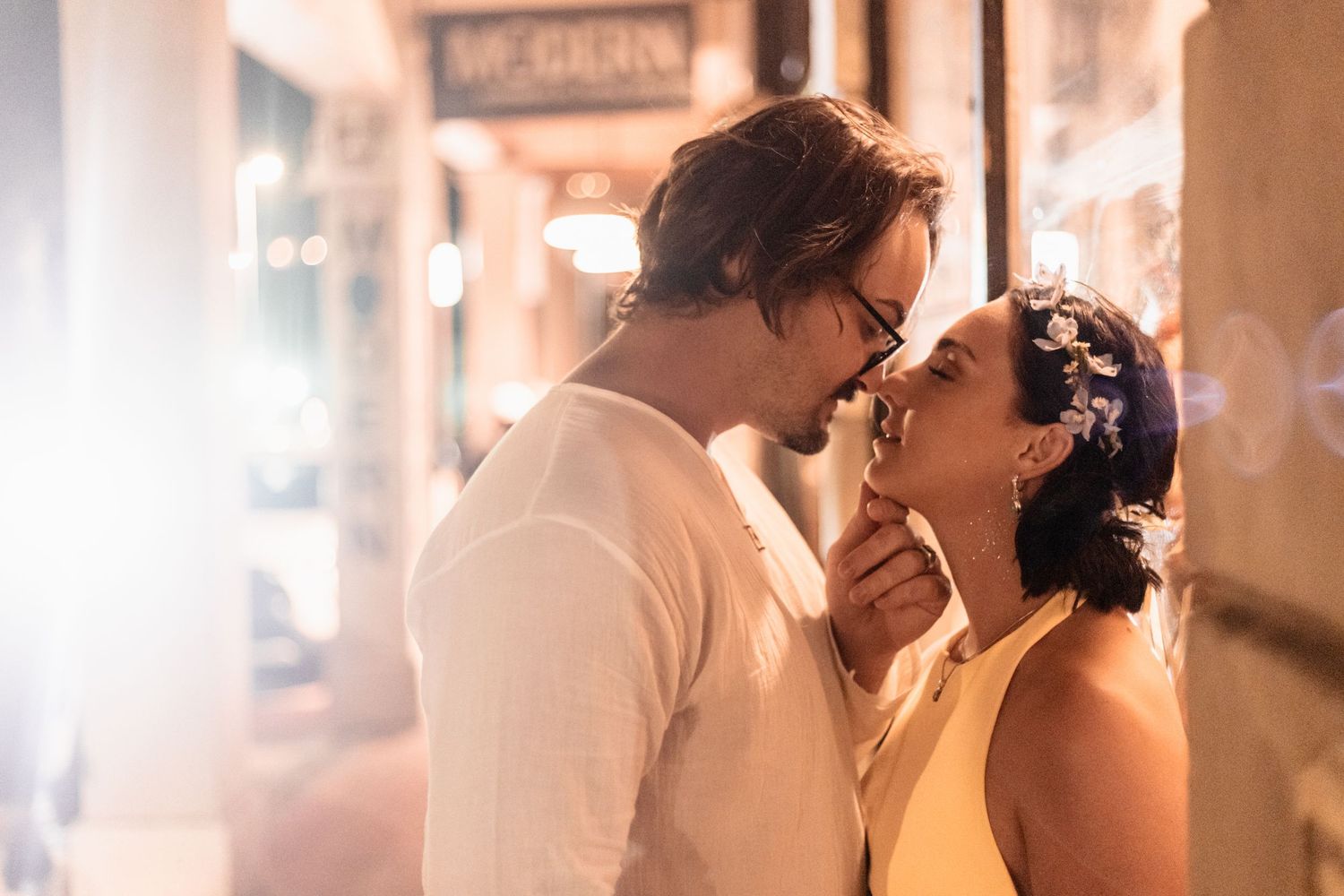 Romantic couple sharing an intimate moment under soft lighting with bride wearing a floral crown in evening setting.