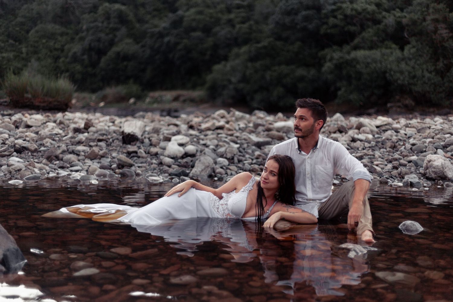 A series of romantic wedding photos showing a couple in white attire posing near a rocky riverbed.