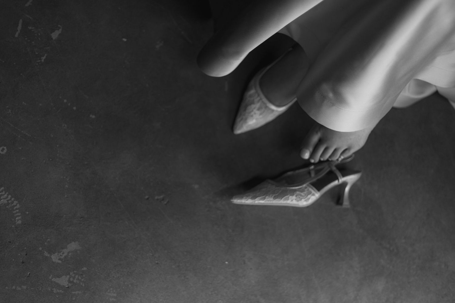 Black and white photo of a woman's feet in elegant heeled mules on a dark floor.