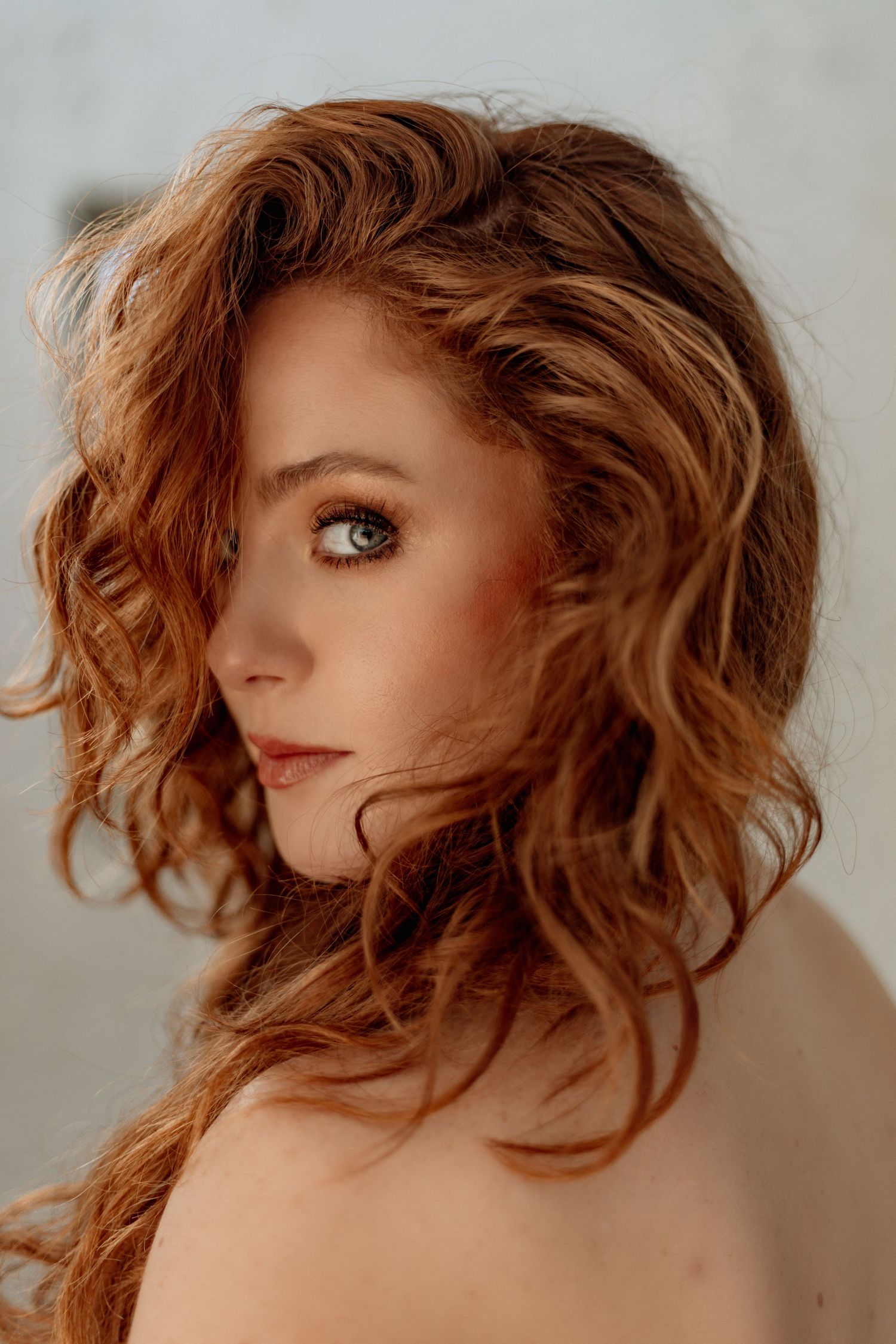 A portrait showing golden wavy hair and striking blue eyes in a warm, soft-focus style.